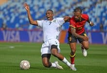 An intense soccer game featuring two athletes competing fiercely for the ball on the field. One player in a white jersey and the other in a red jersey are chasing the ball, showcasing agility and determination.