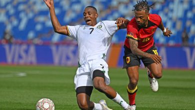 An intense soccer game featuring two athletes competing fiercely for the ball on the field. One player in a white jersey and the other in a red jersey are chasing the ball, showcasing agility and determination.