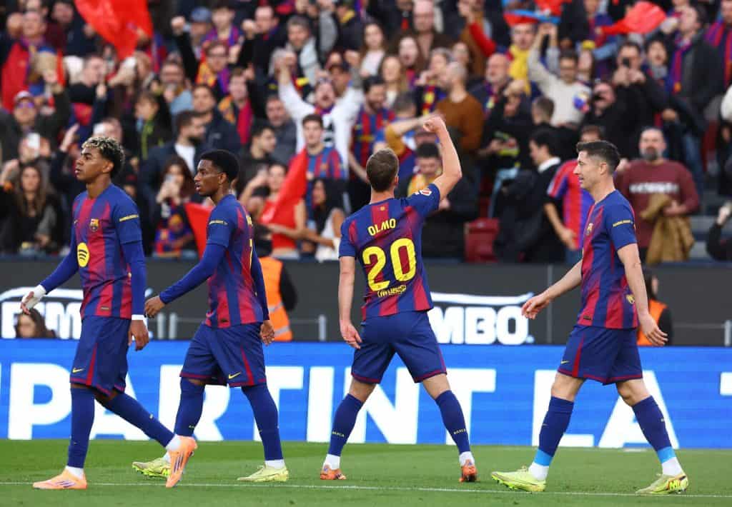Brightly colored soccer players in action on the pitch with enthusiastic crowd cheering in the background.