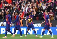 Brightly colored soccer players in action on the pitch with enthusiastic crowd cheering in the background.