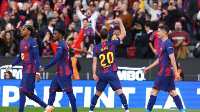 Brightly colored soccer players in action on the pitch with enthusiastic crowd cheering in the background.