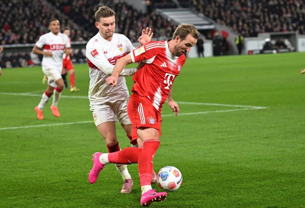 A Bayern Munich player in red jersey defending against VfB Stuttgart player in white jersey during a soccer game.