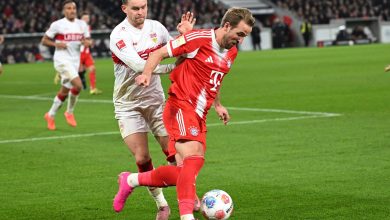A Bayern Munich player in red jersey defending against VfB Stuttgart player in white jersey during a soccer game.