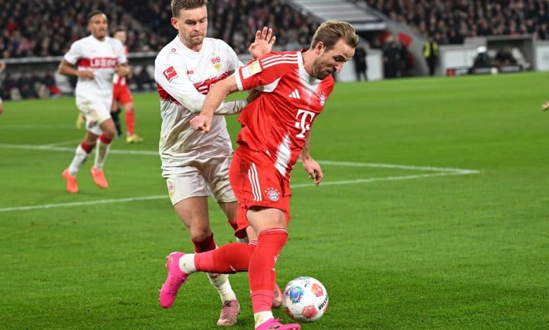 A Bayern Munich player in red jersey defending against VfB Stuttgart player in white jersey during a soccer game.