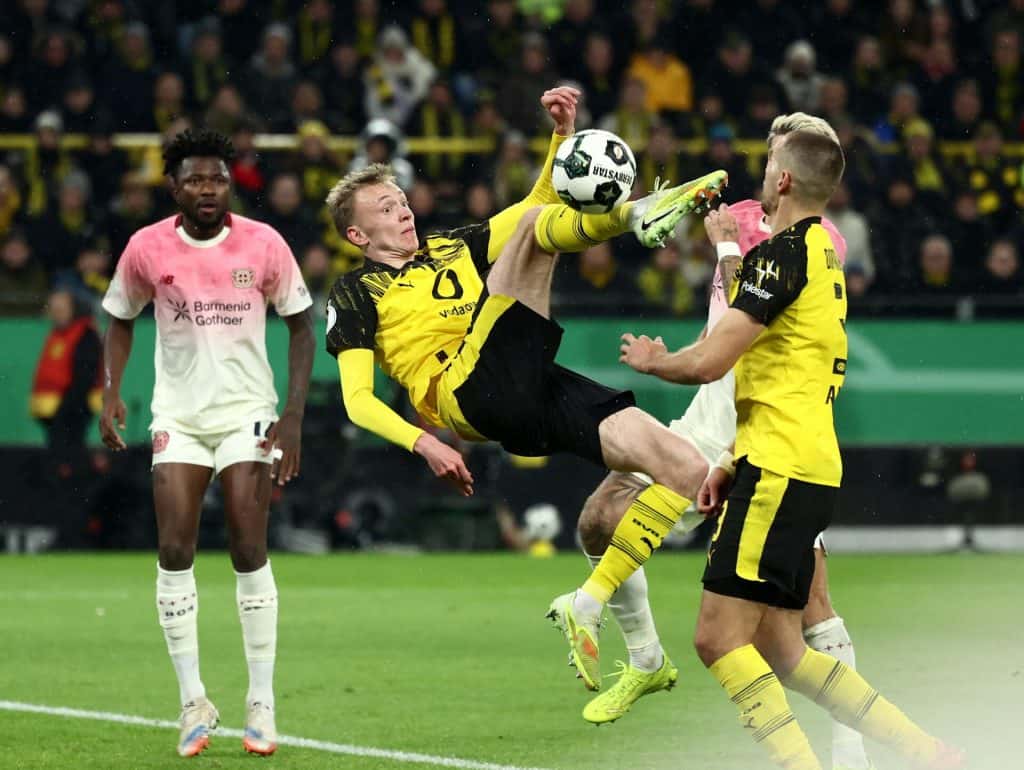 Young football players in yellow and black jerseys and opponents in white and pink jerseys competing fiercely for control of the ball.