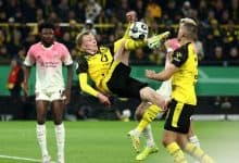 Young football players in yellow and black jerseys and opponents in white and pink jerseys competing fiercely for control of the ball.