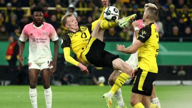 Young football players in yellow and black jerseys and opponents in white and pink jerseys competing fiercely for control of the ball.