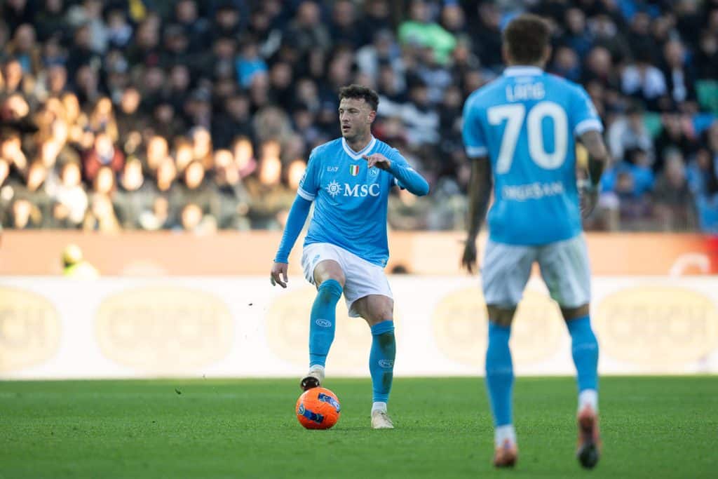 Athletic soccer player in blue uniform controlling the ball during a match with a large crowd watching, showcasing sportsmanship and competitive spirit.