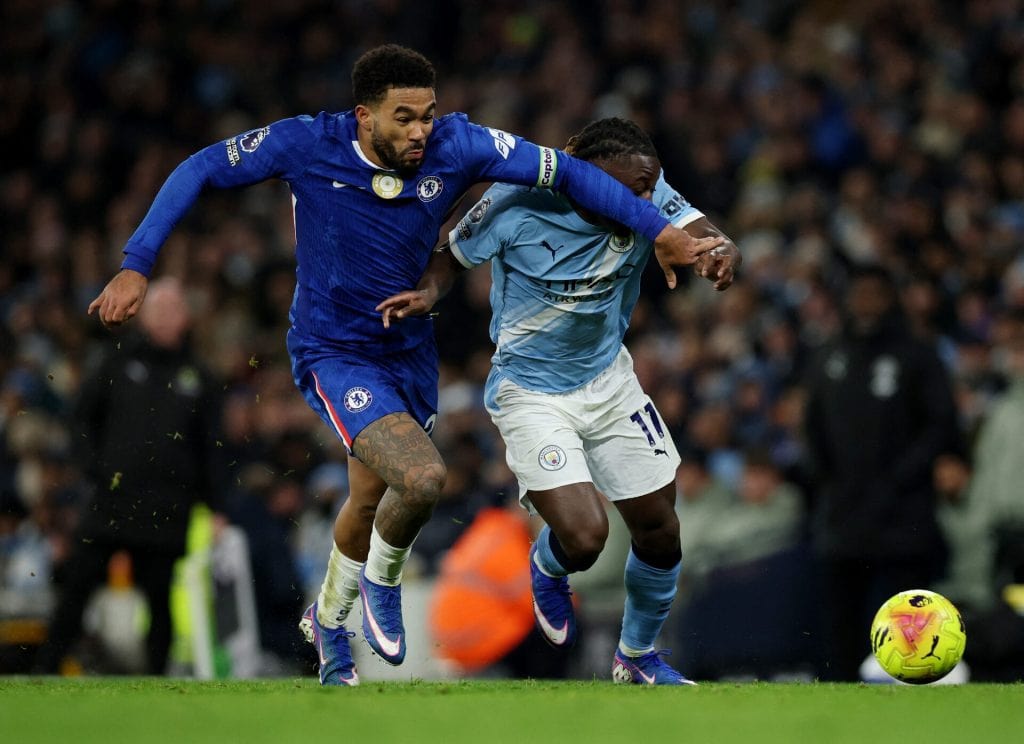 A Chelsea player and a Manchester City player compete fiercely for control of the ball during a high-intensity soccer game.