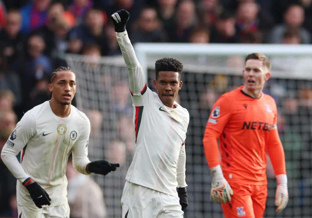 Professional soccer player in action, wearing a white Juventus jersey, raising his hand in a gesture of victory amid a lively game.