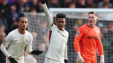 Professional soccer player in action, wearing a white Juventus jersey, raising his hand in a gesture of victory amid a lively game.