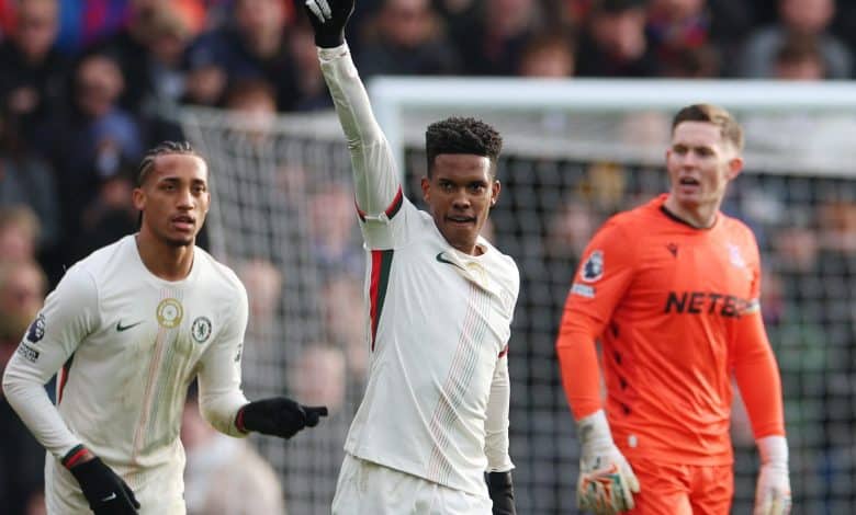 Professional soccer player in action, wearing a white Juventus jersey, raising his hand in a gesture of victory amid a lively game.
