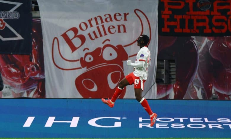Athletic football player jumping in celebration on the field during a game, with advertising banners in the background.