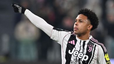Soccer player in Juventus kit raising arm during match, focused on game, with blurred stadium background.