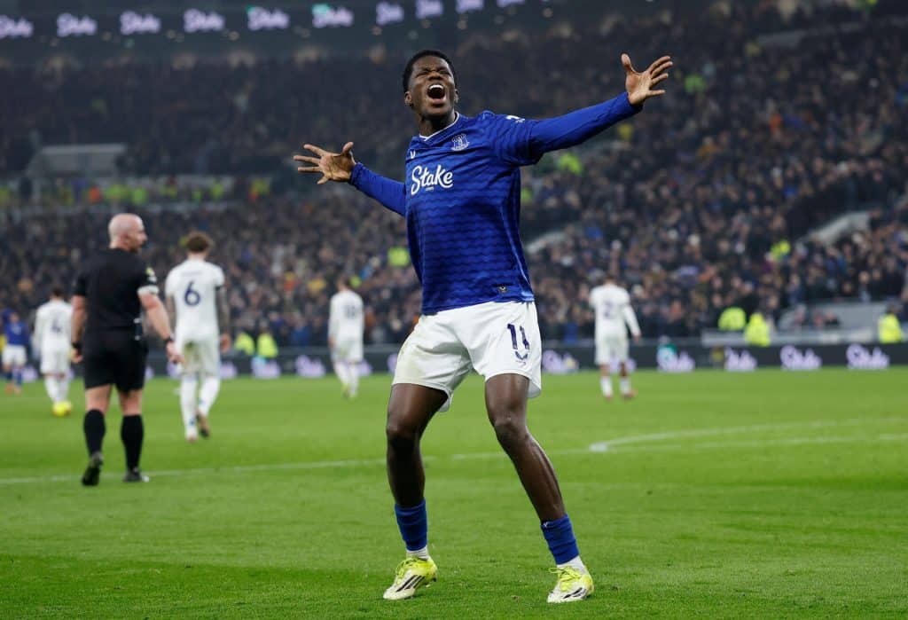 Dynamic soccer player in blue jersey expressing excitement during a match, crowd cheering in the background, sports action captured at a major football game.