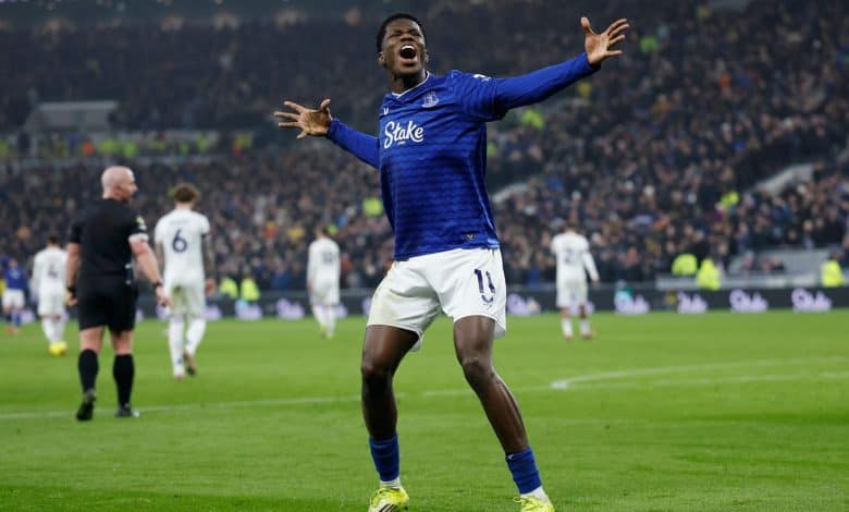 Dynamic soccer player in blue jersey expressing excitement during a match, crowd cheering in the background, sports action captured at a major football game.