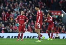 Liverpool football team, players in red kits during match, with fans and stadium in background.