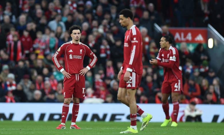 Liverpool football team, players in red kits during match, with fans and stadium in background.