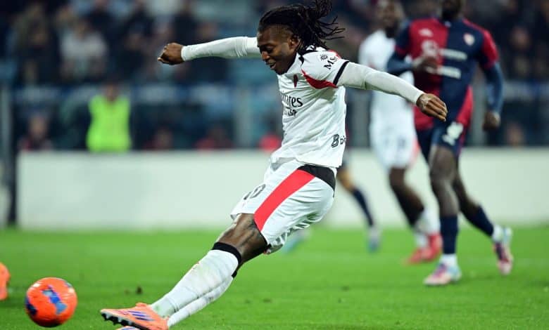 Soccer player in action, kicking the ball on the field with opposing players in the background.