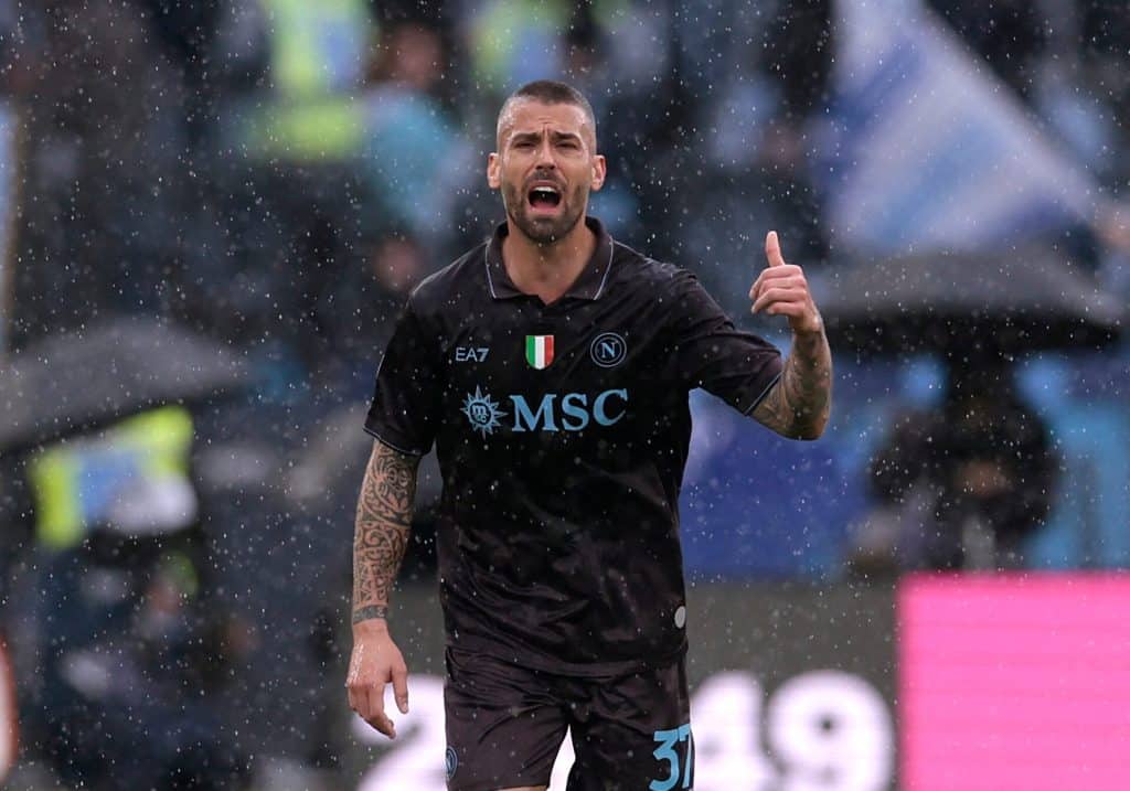 High-action shot of a footballer celebrating on the field during a rainy match, showcasing passion and athleticism, with fans in the background.