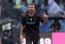 High-action shot of a footballer celebrating on the field during a rainy match, showcasing passion and athleticism, with fans in the background.