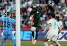 Ethiopian soccer player in green jersey scoring a goal as opponents and goalkeeper look on during exciting match.