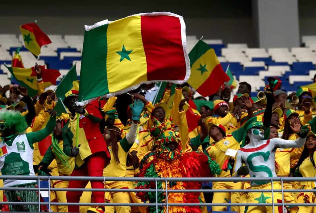 Senegal football fans waving flags, dressed in yellow, green, and red, rally together for their team at a stadium, embodying passion, patriotism, and team spirit.