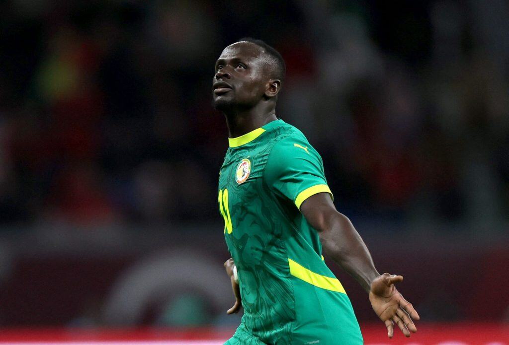 Athletic soccer player celebrating on the field during a match, wearing a green and yellow jersey representing Senegal national team, in a dynamic action shot.