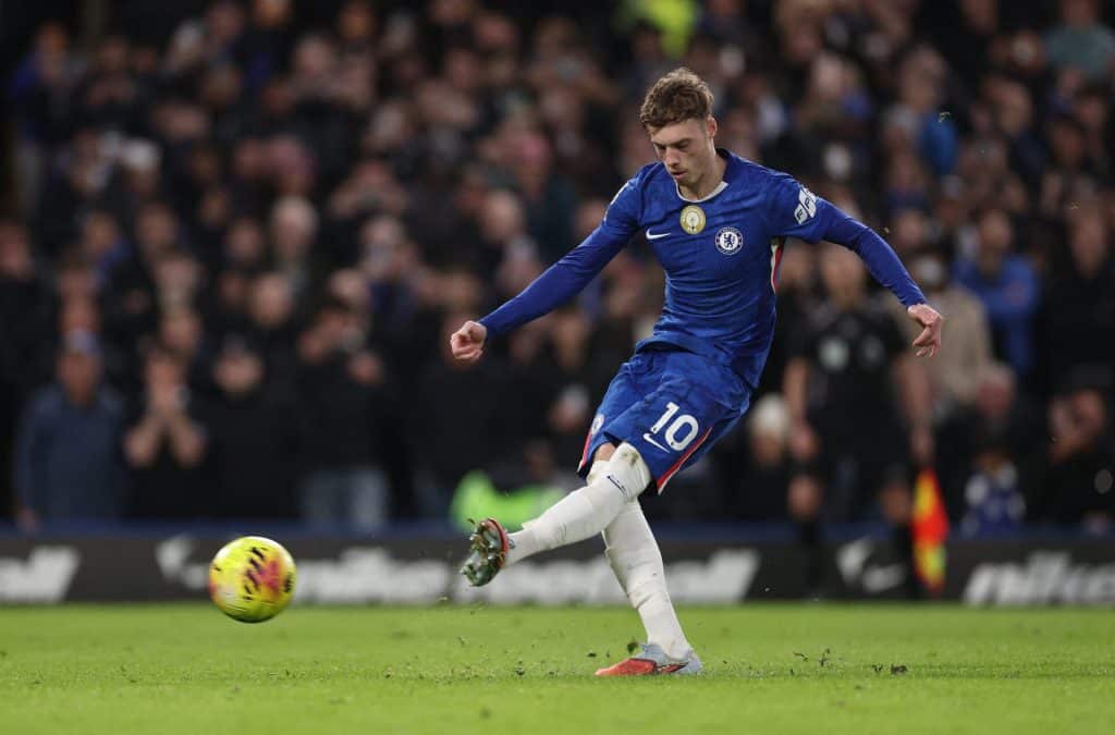 Soccer player in blue jersey kicking football in match, demonstrating skill and agility on the field, with a vibrant crowd watching in the background.
