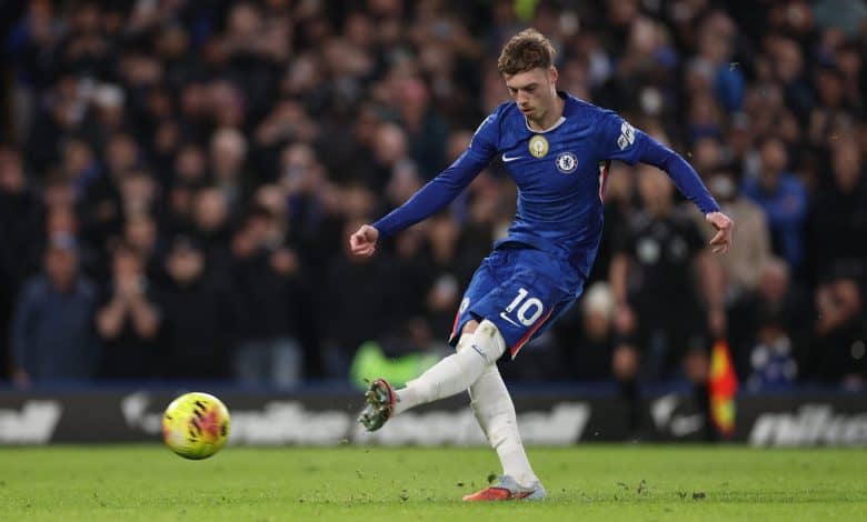 Soccer player in blue jersey kicking football in match, demonstrating skill and agility on the field, with a vibrant crowd watching in the background.