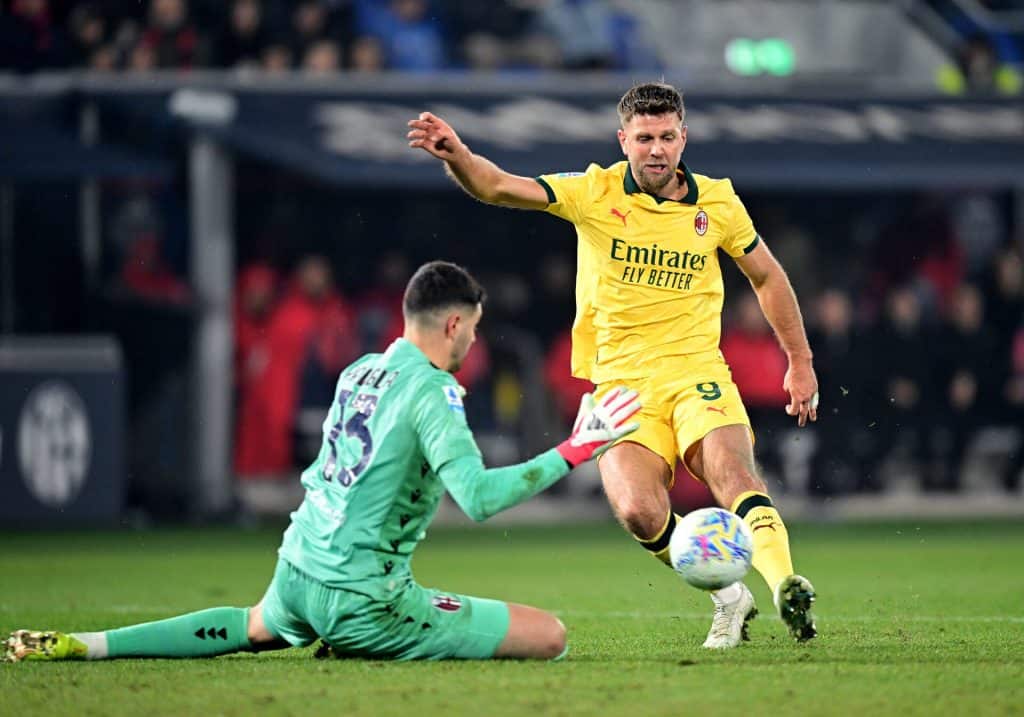 Player in yellow jersey kicking ball past goalkeeper in green kit.