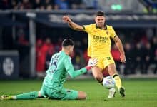 Player in yellow jersey kicking ball past goalkeeper in green kit.