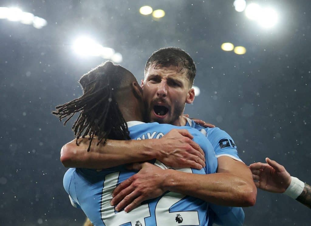 Two football players embracing in celebration after scoring, under stadium lights, during a match.