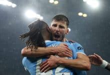Two football players embracing in celebration after scoring, under stadium lights, during a match.