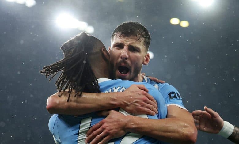 Two football players embracing in celebration after scoring, under stadium lights, during a match.