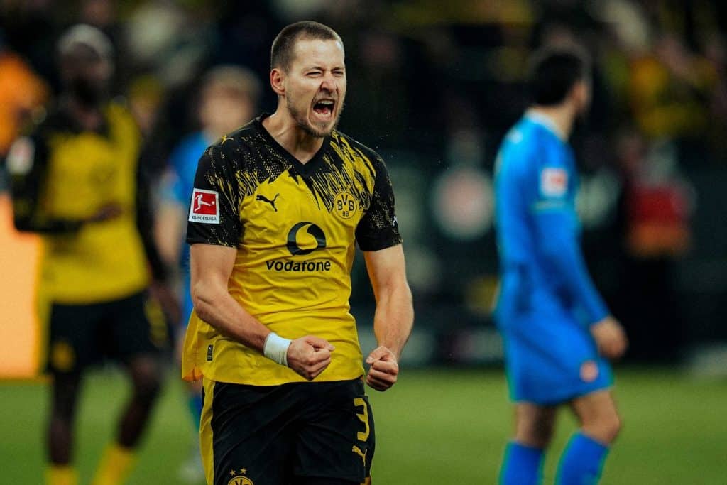 Bright yellow and black sports jersey with Puma and Vodafone logos visible. Background blurred crowd, emphasizing player’s intense expression.