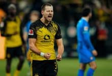 Bright yellow and black sports jersey with Puma and Vodafone logos visible. Background blurred crowd, emphasizing player’s intense expression.