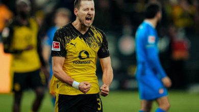 Bright yellow and black sports jersey with Puma and Vodafone logos visible. Background blurred crowd, emphasizing player’s intense expression.