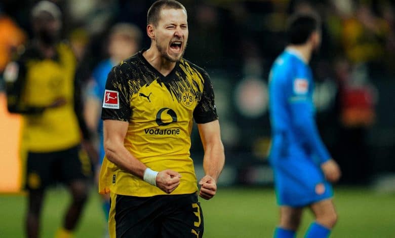 Bright yellow and black sports jersey with Puma and Vodafone logos visible. Background blurred crowd, emphasizing player’s intense expression.
