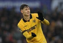 Football player celebrating victory in rain, wearing yellow jersey with sponsor logos, during match.