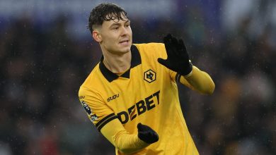 Football player celebrating victory in rain, wearing yellow jersey with sponsor logos, during match.