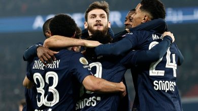 Group of soccer players celebrating together on the field after scoring a goal, wearing navy blue jerseys with numbers and sponsor logos.