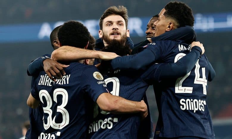 Group of soccer players celebrating together on the field after scoring a goal, wearing navy blue jerseys with numbers and sponsor logos.