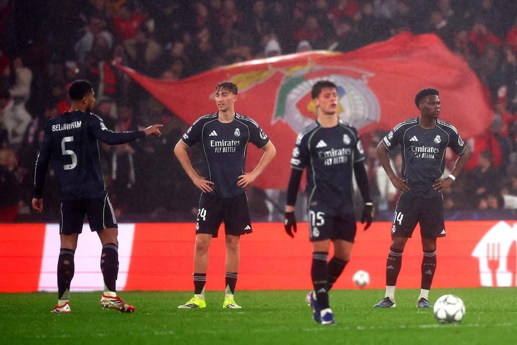 Football players in black jerseys celebrating on the field with a large flag in the background.