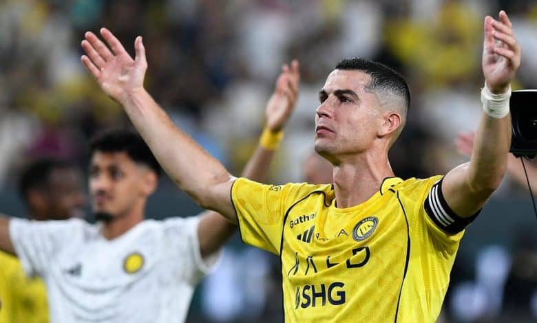 Football player in yellow jersey celebrating on the field with arms raised, surrounded by fans and teammates, during a match.